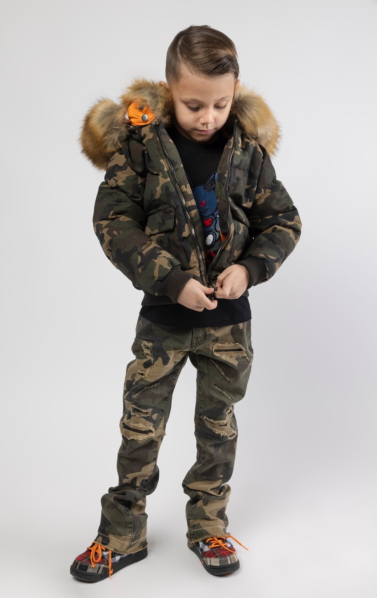 Full zip bomber jacket silhouette, with quilted padding and dense insulation for extreme warmth. Made with 100% polyester lining and featuring a removable faux jackal fur collar and hood. Available in woodland and black camo.