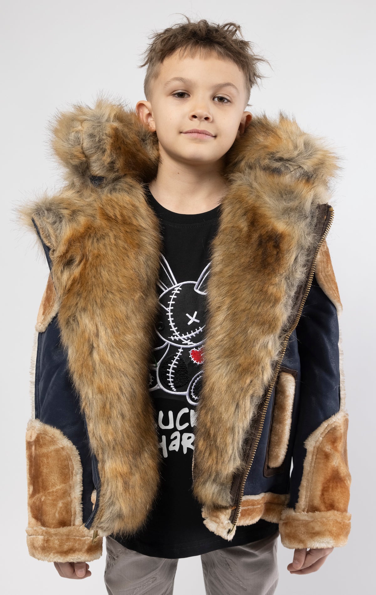 Faux suede body. Soft faux shearling lining on the body, sleeves, and pockets. Toggle front closure with vegan suede straps and a buckle at the neck. Detachable hood made of faux fox fur with a zipper.