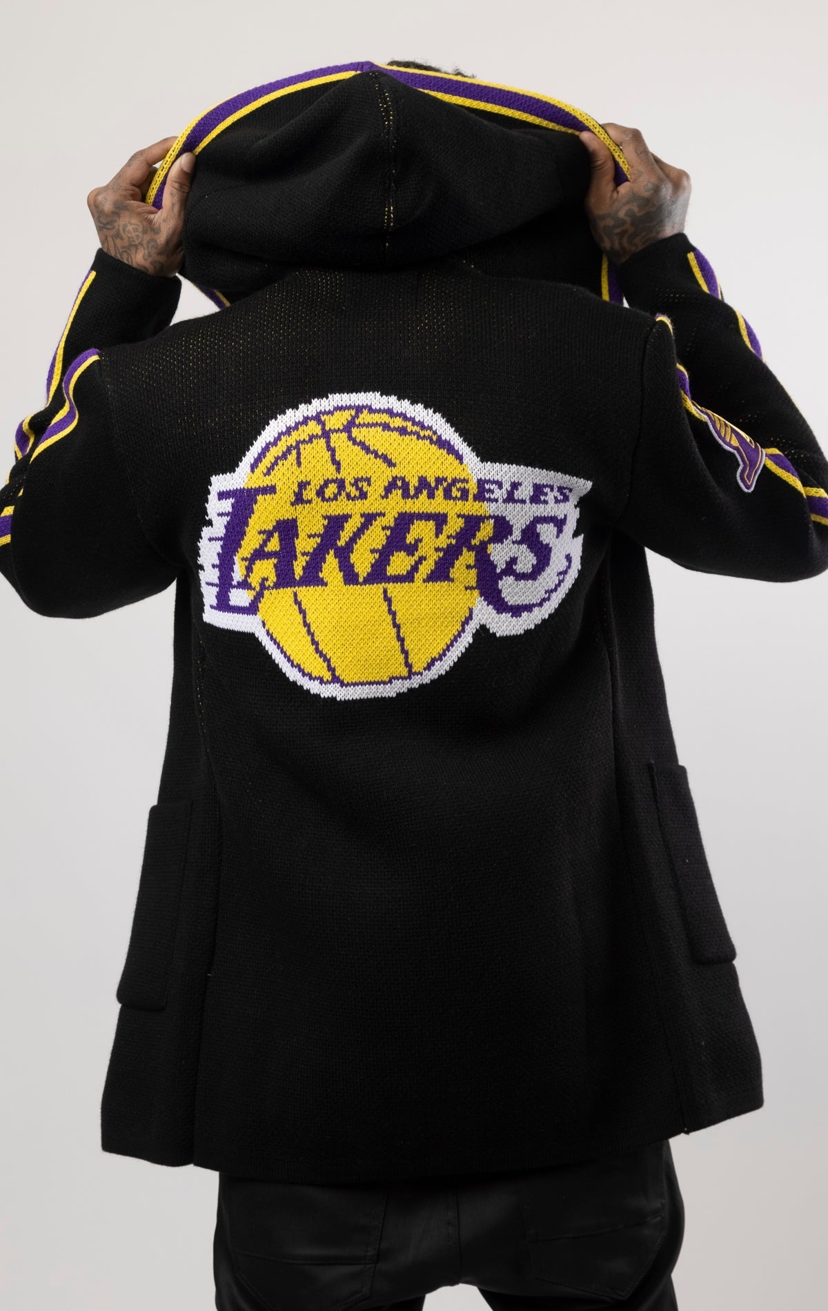 black LA LAKERS Cardigan Sweater. This cozy jacket is designed with a stylish three-quarter length and boasts bold team branding on the front, back, and sleeve. Complete with a full-zip closure, attached hood, and front pockets, this knit sweater offers b