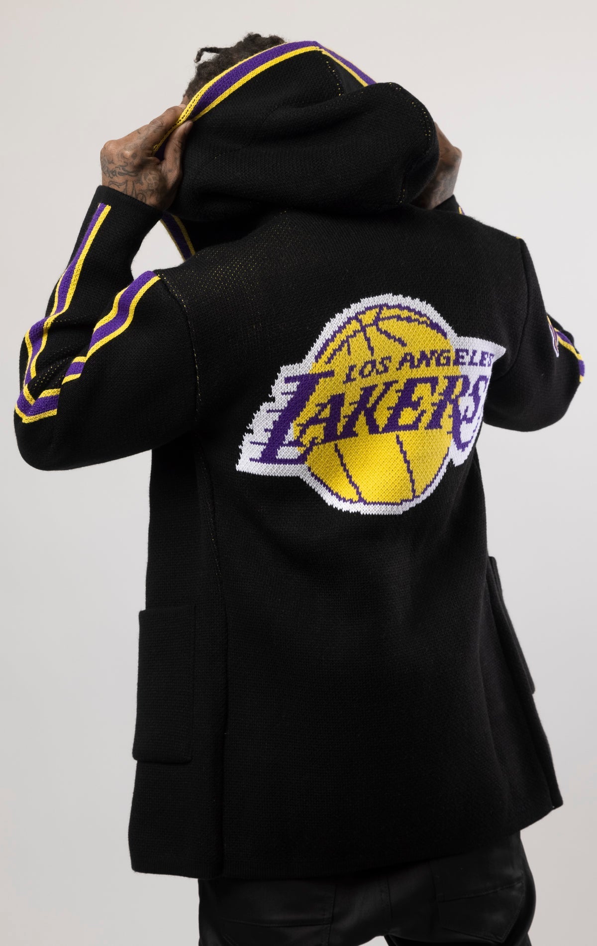 black LA LAKERS Cardigan Sweater. This cozy jacket is designed with a stylish three-quarter length and boasts bold team branding on the front, back, and sleeve. Complete with a full-zip closure, attached hood, and front pockets, this knit sweater offers b