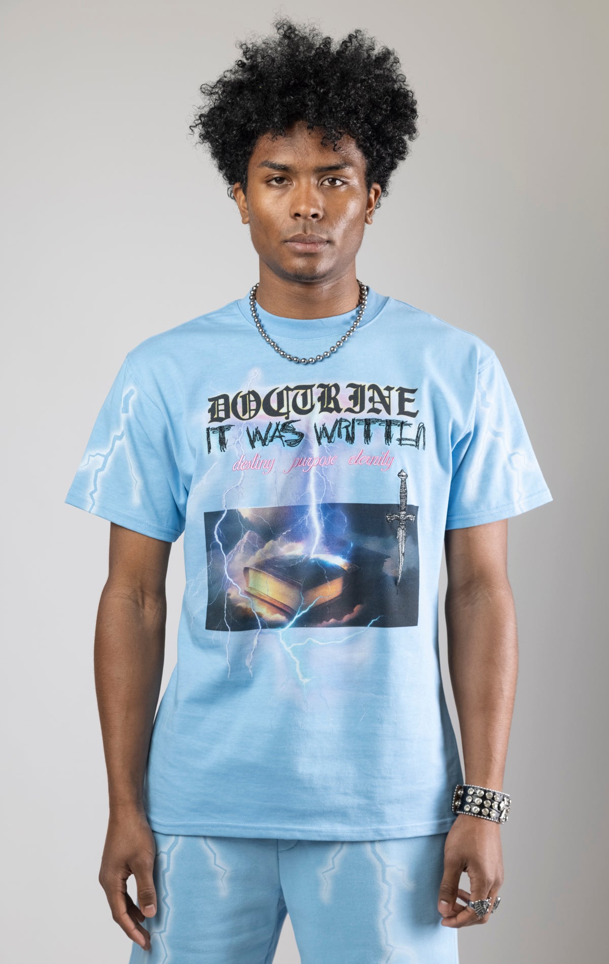 Sky blue t-shirt with a digital photo print on the front and back, embroidered text on the front, and a 3D metallic dagger embroidered on the back.