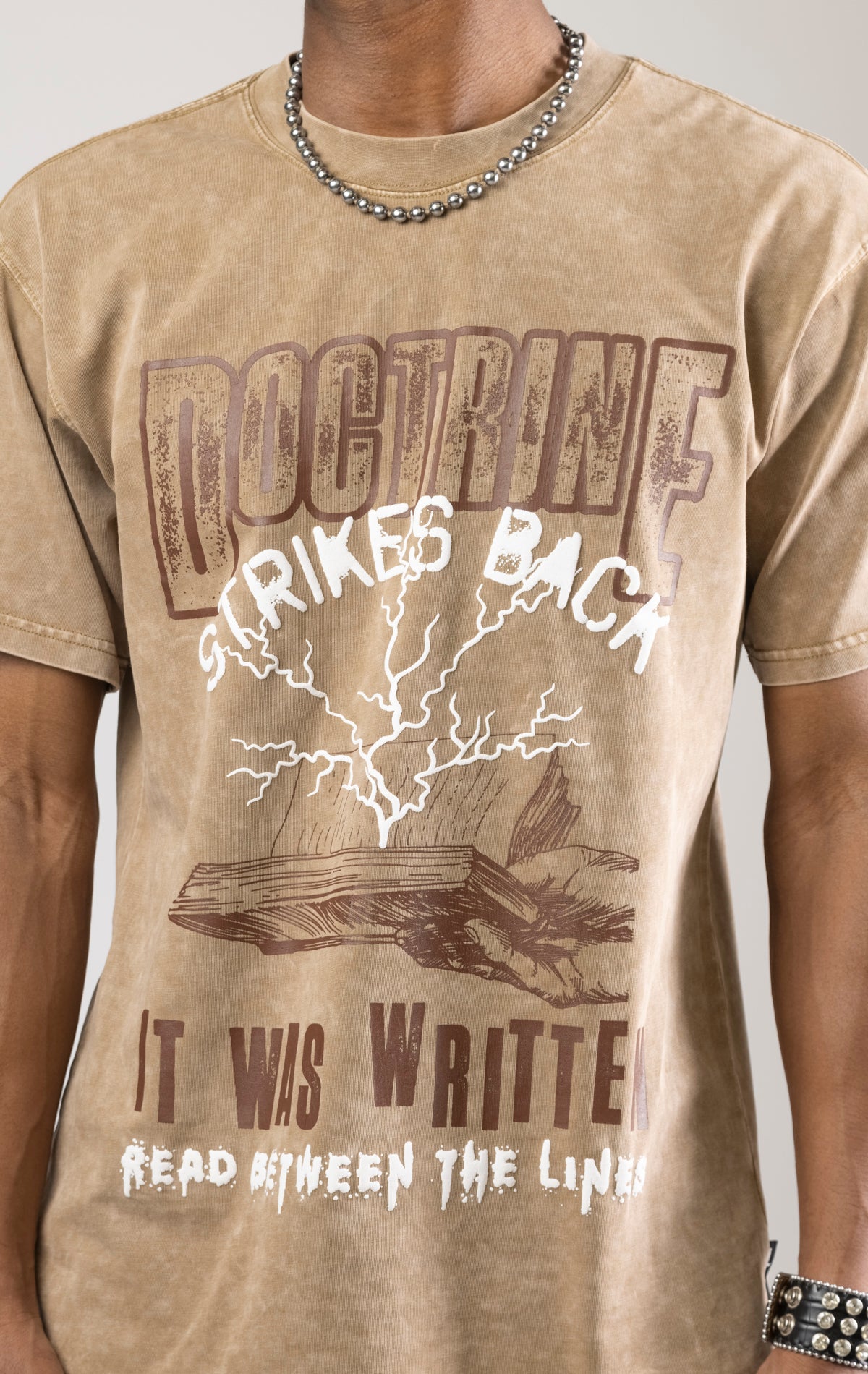 A DOCTRINE STRIKE BACK T-shirt featuring a high-definition digital graphic print across the front. The shirt is made from 100% cotton and has a vintage-washed look.