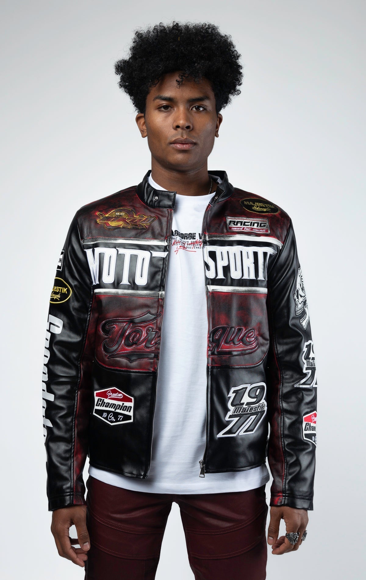 Black motor sport racing jacket with snap-button collar, full zip-up closure, multi-patch and embroidered details, zippered sleeves and pockets, and elasticized ribbed collar, cuffs, and waist. The interior includes a hanger loop, welt pocket, and faux le