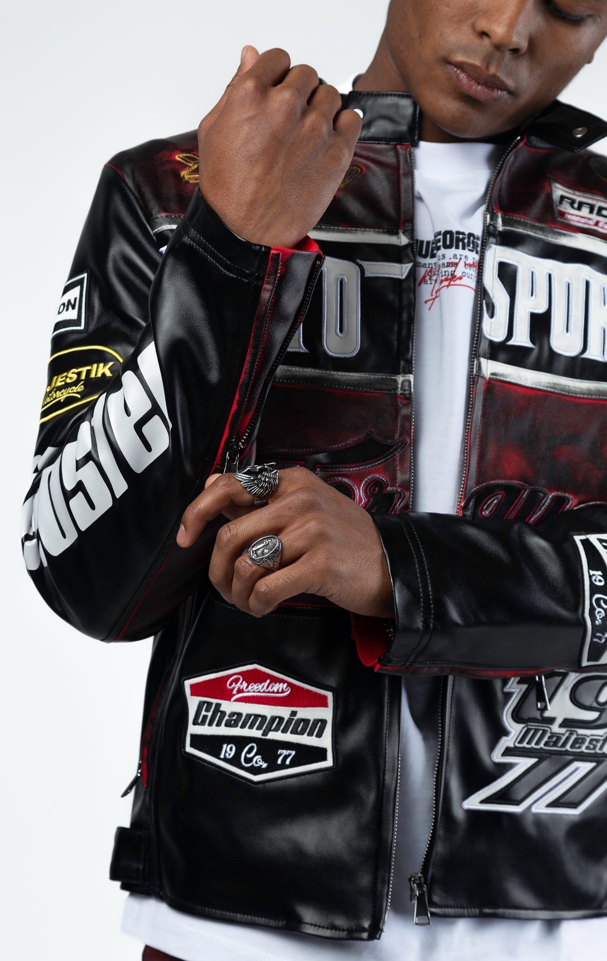 Black motor sport racing jacket with snap-button collar, full zip-up closure, multi-patch and embroidered details, zippered sleeves and pockets, and elasticized ribbed collar, cuffs, and waist. The interior includes a hanger loop, welt pocket, and faux le