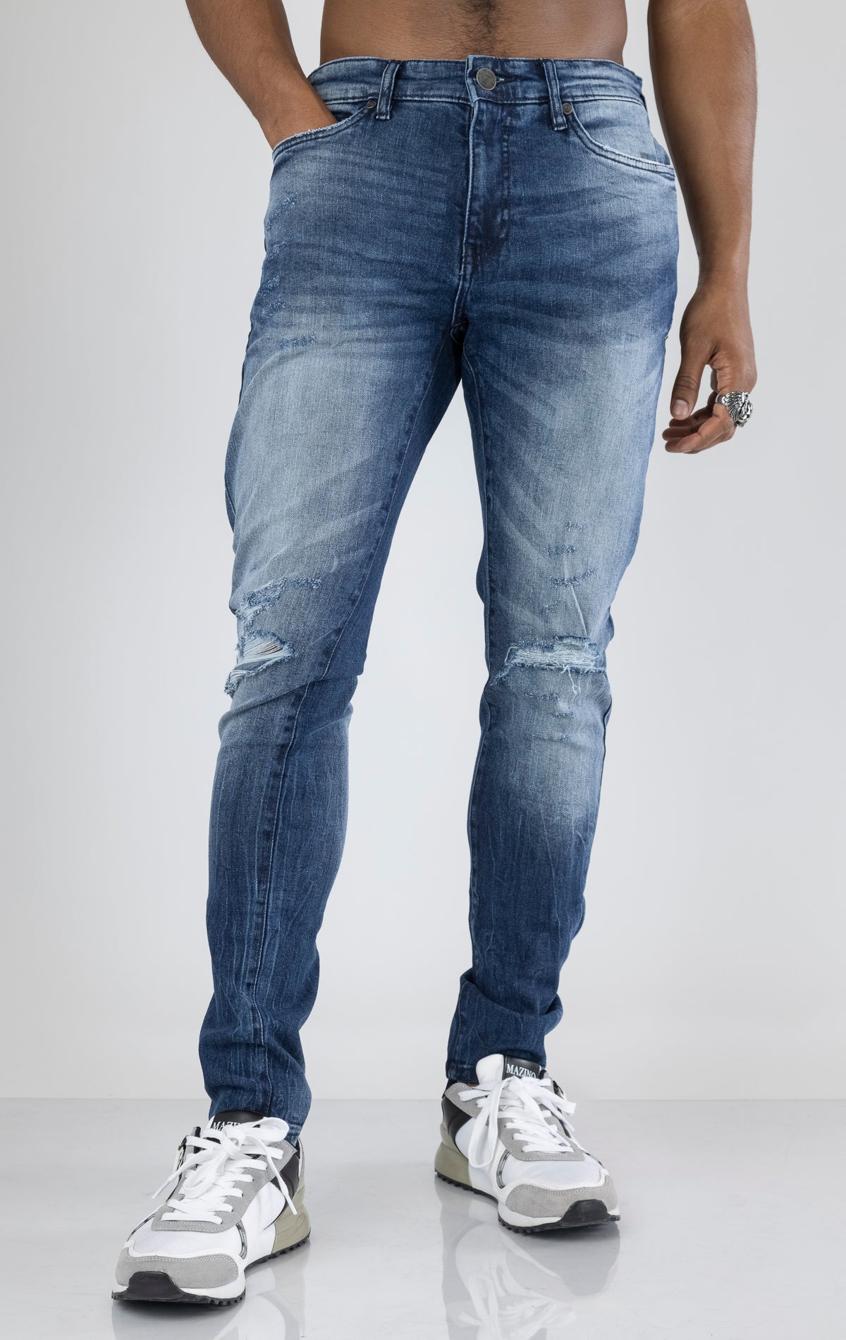 Men's ripped and distressed denim pants in a variety of washes. The pants feature a regular rise, tapered fit from the knee down, open rips at the knees, unique distressing details, and are made from 98% cotton with 2% lycra for stretch