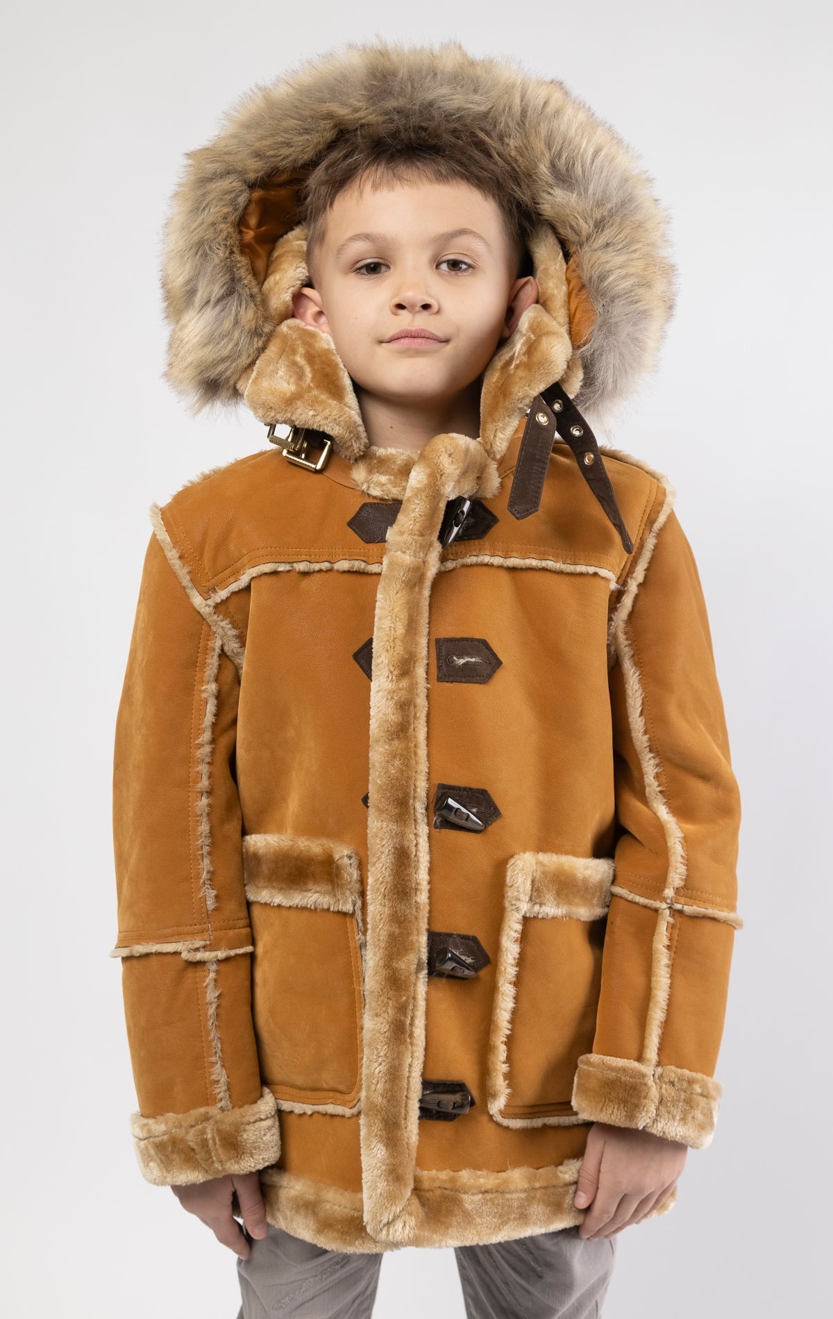 Cognac jacket lined with plush faux shearling throughout the body and sleeves. It also features shearling-accented pockets, a horn toggle front closure, and vegan suede straps with a buckle at the neck. For added convenience, a detachable faux fox fur hoo