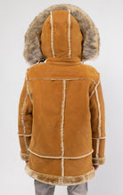 Cognac jacket lined with plush faux shearling throughout the body and sleeves. It also features shearling-accented pockets, a horn toggle front closure, and vegan suede straps with a buckle at the neck. For added convenience, a detachable faux fox fur hood with a zipper is included. This product is also available for adults.