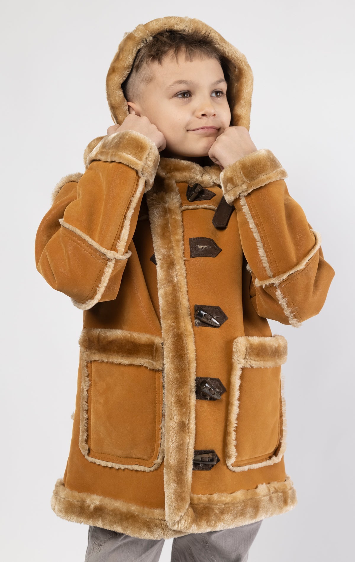 Cognac jacket lined with plush faux shearling throughout the body and sleeves. It also features shearling-accented pockets, a horn toggle front closure, and vegan suede straps with a buckle at the neck. For added convenience, a detachable faux fox fur hoo