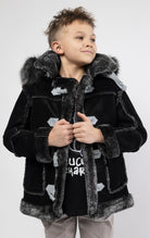 Black jacket lined with plush faux shearling throughout the body and sleeves. It also features shearling-accented pockets, a horn toggle front closure, and vegan suede straps with a buckle at the neck. For added convenience, a detachable faux fox fur hood