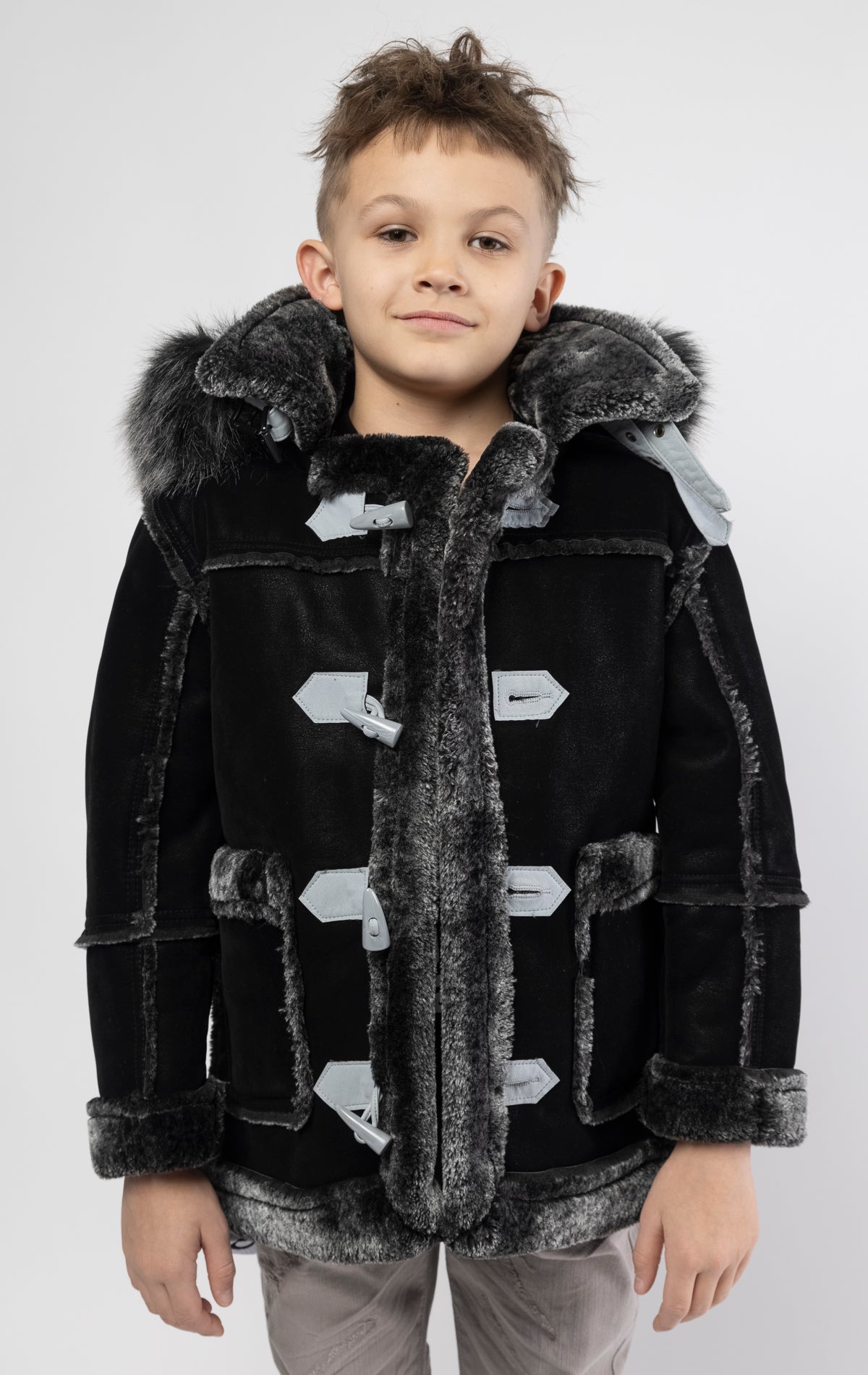 Black jacket lined with plush faux shearling throughout the body and sleeves. It also features shearling-accented pockets, a horn toggle front closure, and vegan suede straps with a buckle at the neck. For added convenience, a detachable faux fox fur hood