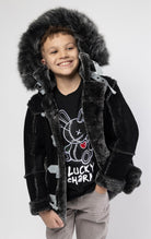 Black jacket lined with plush faux shearling throughout the body and sleeves. It also features shearling-accented pockets, a horn toggle front closure, and vegan suede straps with a buckle at the neck. For added convenience, a detachable faux fox fur hood