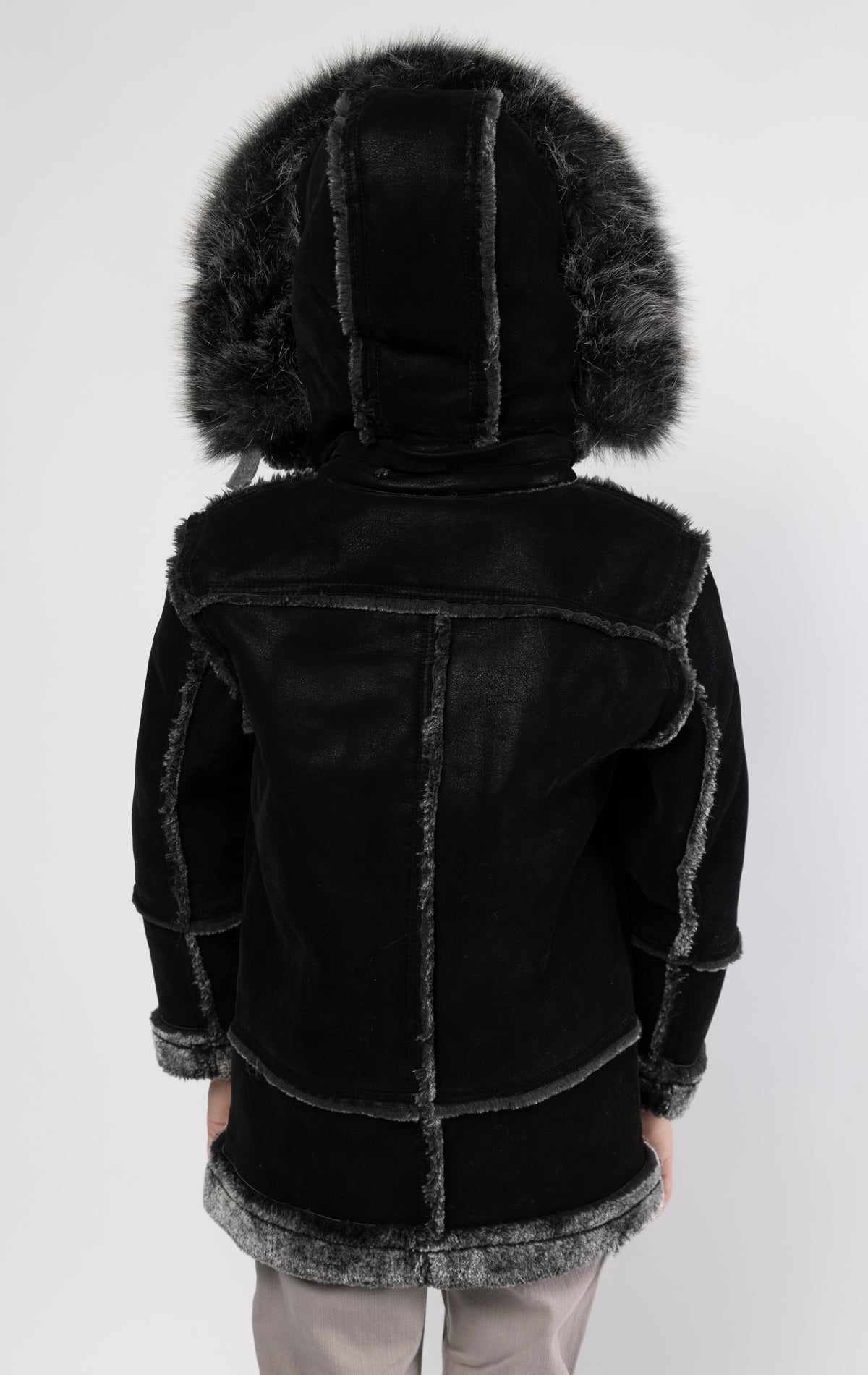 Black jacket lined with plush faux shearling throughout the body and sleeves. It also features shearling-accented pockets, a horn toggle front closure, and vegan suede straps with a buckle at the neck. For added convenience, a detachable faux fox fur hood