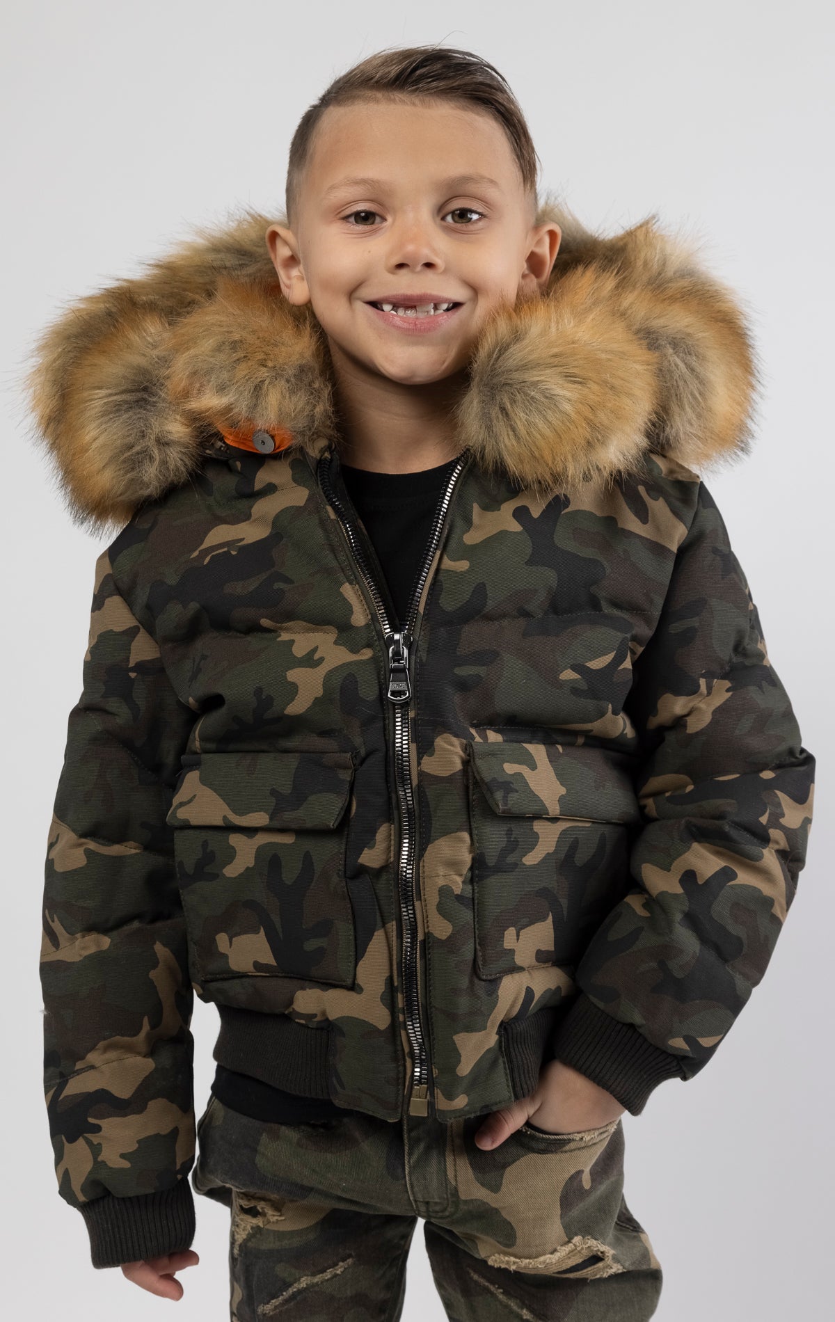 Full zip bomber jacket silhouette, with quilted padding and dense insulation for extreme warmth. Made with 100% polyester lining and featuring a removable faux jackal fur collar and hood. Available in woodland and black camo.
