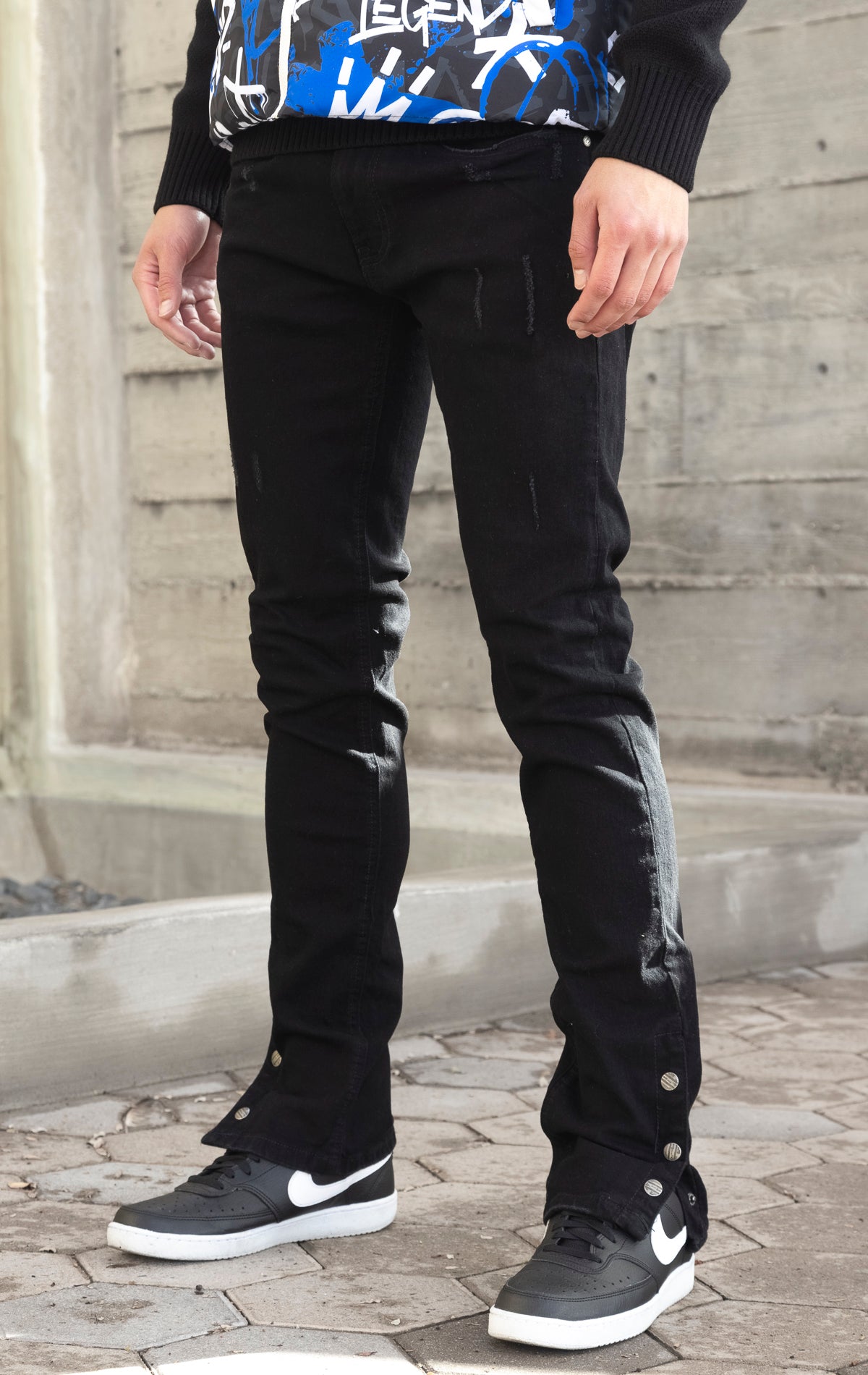 Black denim featuring distressed detailing throughout, a skinny fit, stretch denim, and a buttoned flare.