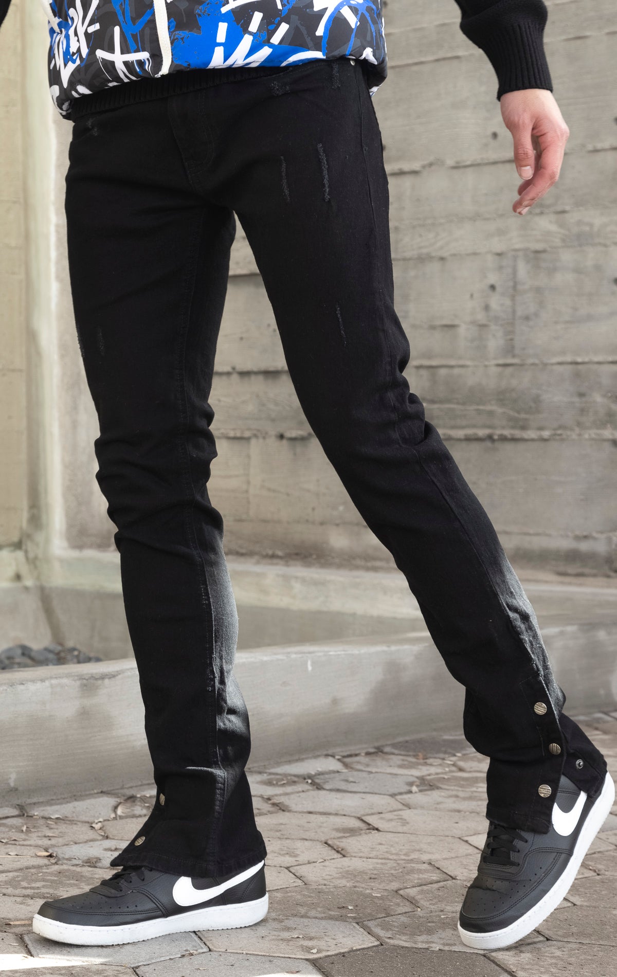 Black denim featuring distressed detailing throughout, a skinny fit, stretch denim, and a buttoned flare.