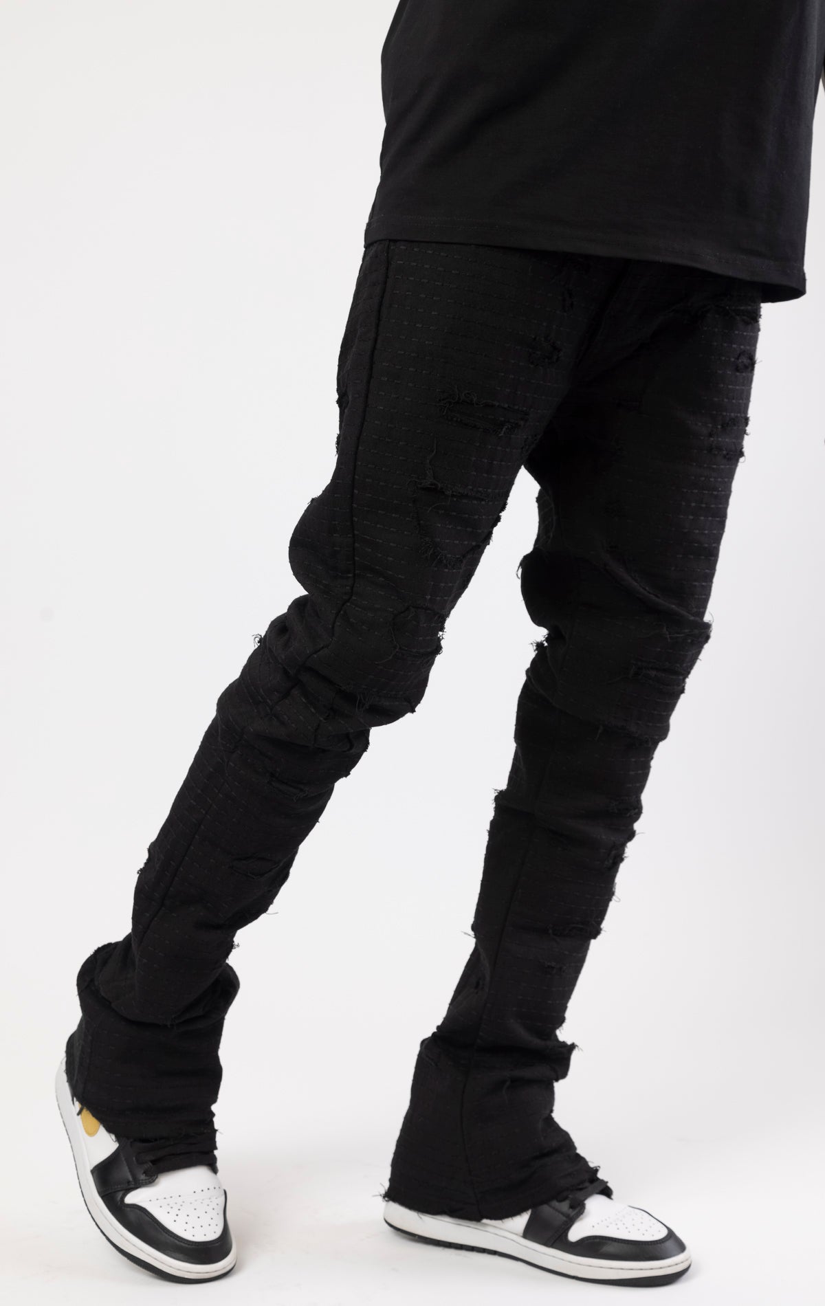 Jet black distressed denim jeans with a ripped and stacked fit.