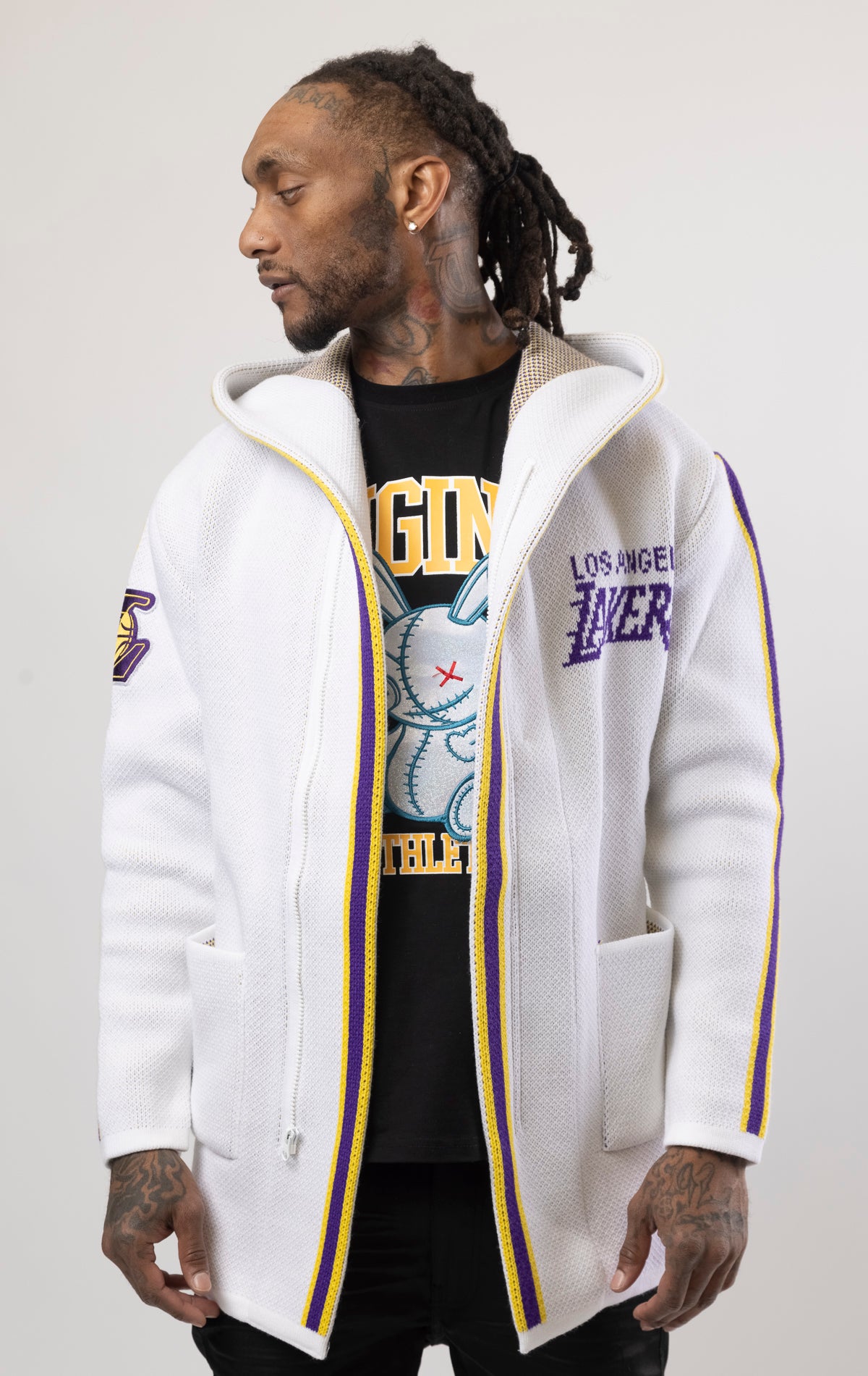White LA LAKERS Cardigan Sweater. This cozy jacket is designed with a stylish three-quarter length and boasts bold team branding on the front, back, and sleeve. Complete with a full-zip closure, attached hood, and front pockets, this knit sweater offers both comfort and style.