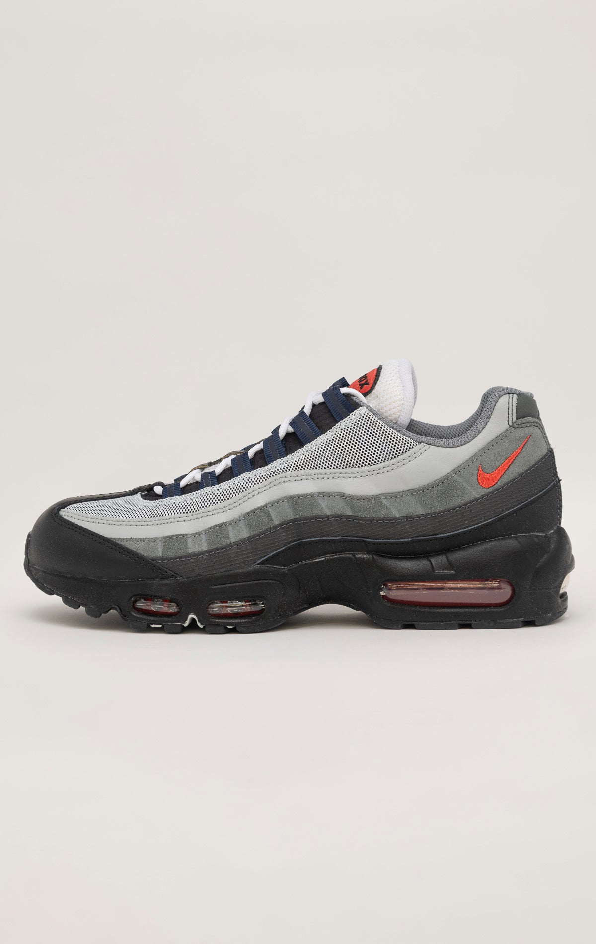 A black Nike Air Max 95 sneaker with a wavy mesh upper and visible Air cushioning units in the heel and forefoot. Anthracite and smoke grey accents contrast with pops of track red for a bold look.