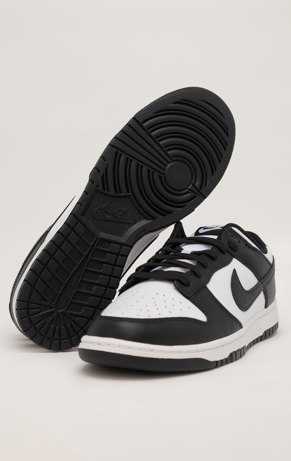 A black and white Nike Dunk Low sneaker. The shoe has a white leather upper with black overlays on the swoosh, heel, and eyelets. The toe box features perforations for ventilation. The tongue is nylon and black with a white Nike logo. The laces are white and the sole is white with a black outsole