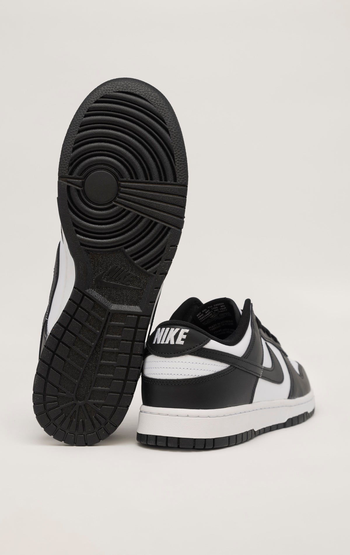 A black and white Nike Dunk Low sneaker. The shoe has a white leather upper with black overlays on the swoosh, heel, and eyelets. The toe box features perforations for ventilation. The tongue is nylon and black with a white Nike logo. The laces are white and the sole is white with a black outsole