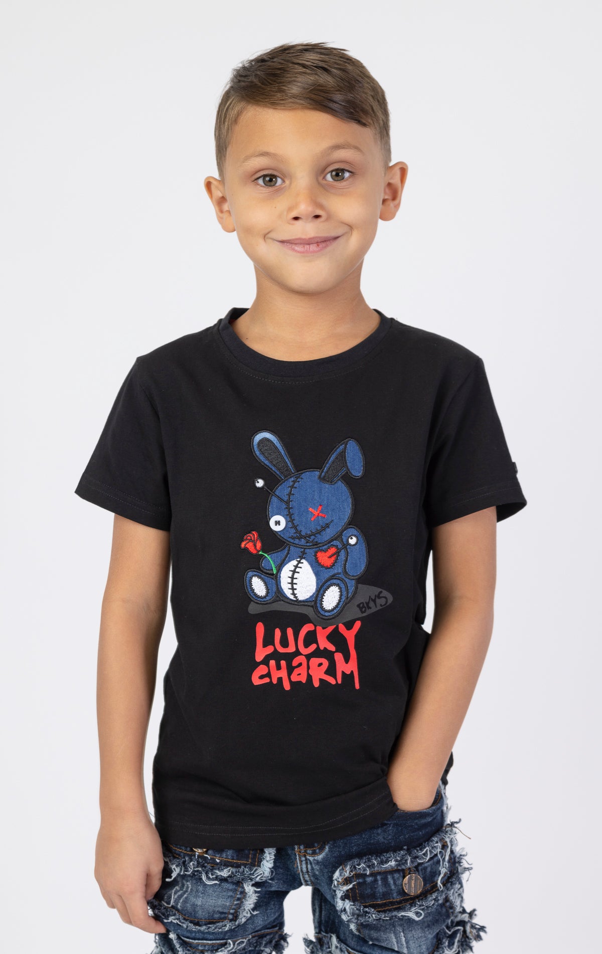 Kids Denim Lucky Charm Black t-shirt. Made from a comfortable blend of 95% cotton and 5% spandex. Features a denim fabric, crew neck, short sleeves, and a lucky charm patch.