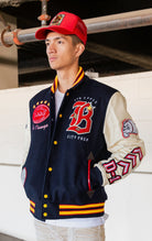 Blue, red and white jacket with leather sleeves, striped ribbed collar, cuffs, and waistband, along with chenille patches and embroidered designs and a snap button front closure