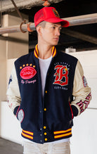 Blue, red and white jacket with leather sleeves, striped ribbed collar, cuffs, and waistband, along with chenille patches and embroidered designs and a snap button front closure