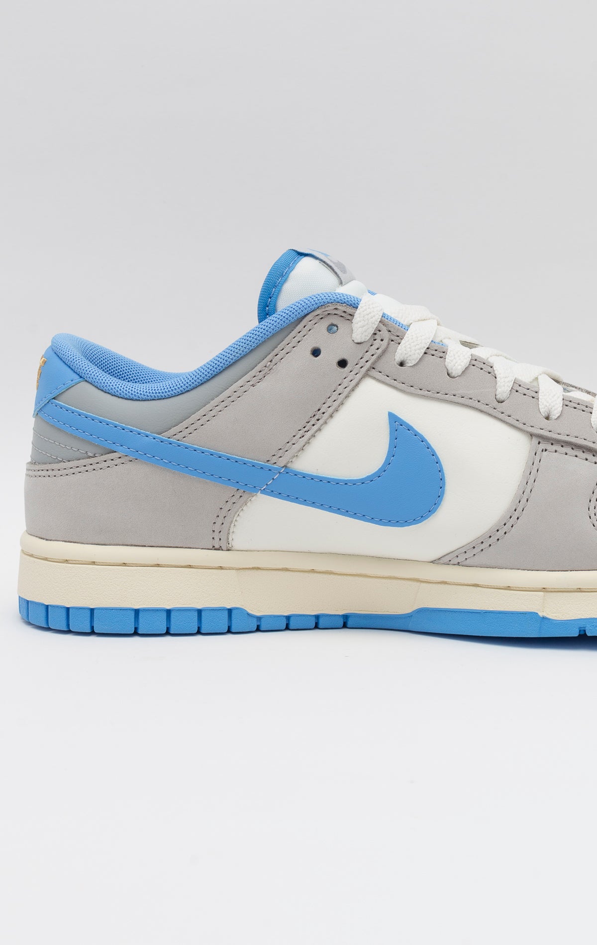 The Nike Dunk Low Athletic Department University Blue showcases a Light Smoke Gray upper with University Blue detailing. Made with high-quality leather and suede, it boasts both durability and fashion in a traditional low-top design. The padded collar, cushioned insole, and pivot point tread on the rubber outsole guarantee comfort. The Light Iron Ore EVA foam midsole offers impact defense. Iconic Swoosh logos can be found on both sides, and the tongue and heel tab feature Nike branding.