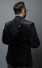 Black, slim-fit velvet blazer adorned with sequins and beads. The blazer has a peak lapel collar, long sleeves, two-button closure, and four-button cuffs. The blazer is made from a blend of 92% regenerated fabric and 8% spandex.