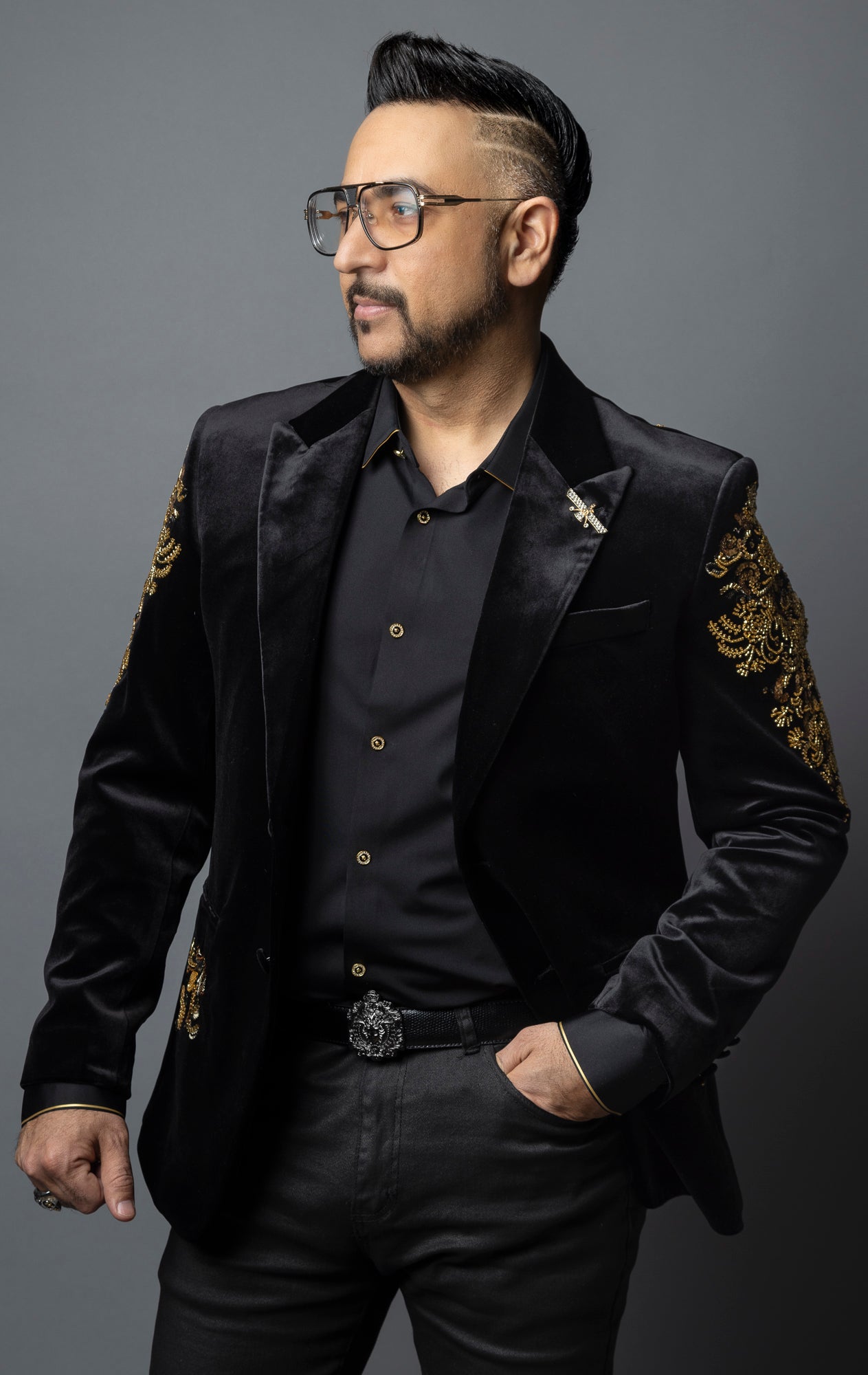 Black, slim-fit velvet blazer adorned with sequins and beads. The blazer has a peak lapel collar, long sleeves, two-button closure, and four-button cuffs. The blazer is made from a blend of 92% regenerated fabric and 8% spandex.