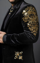 Black, slim-fit velvet blazer adorned with sequins and beads. The blazer has a peak lapel collar, long sleeves, two-button closure, and four-button cuffs. The blazer is made from a blend of 92% regenerated fabric and 8% spandex.