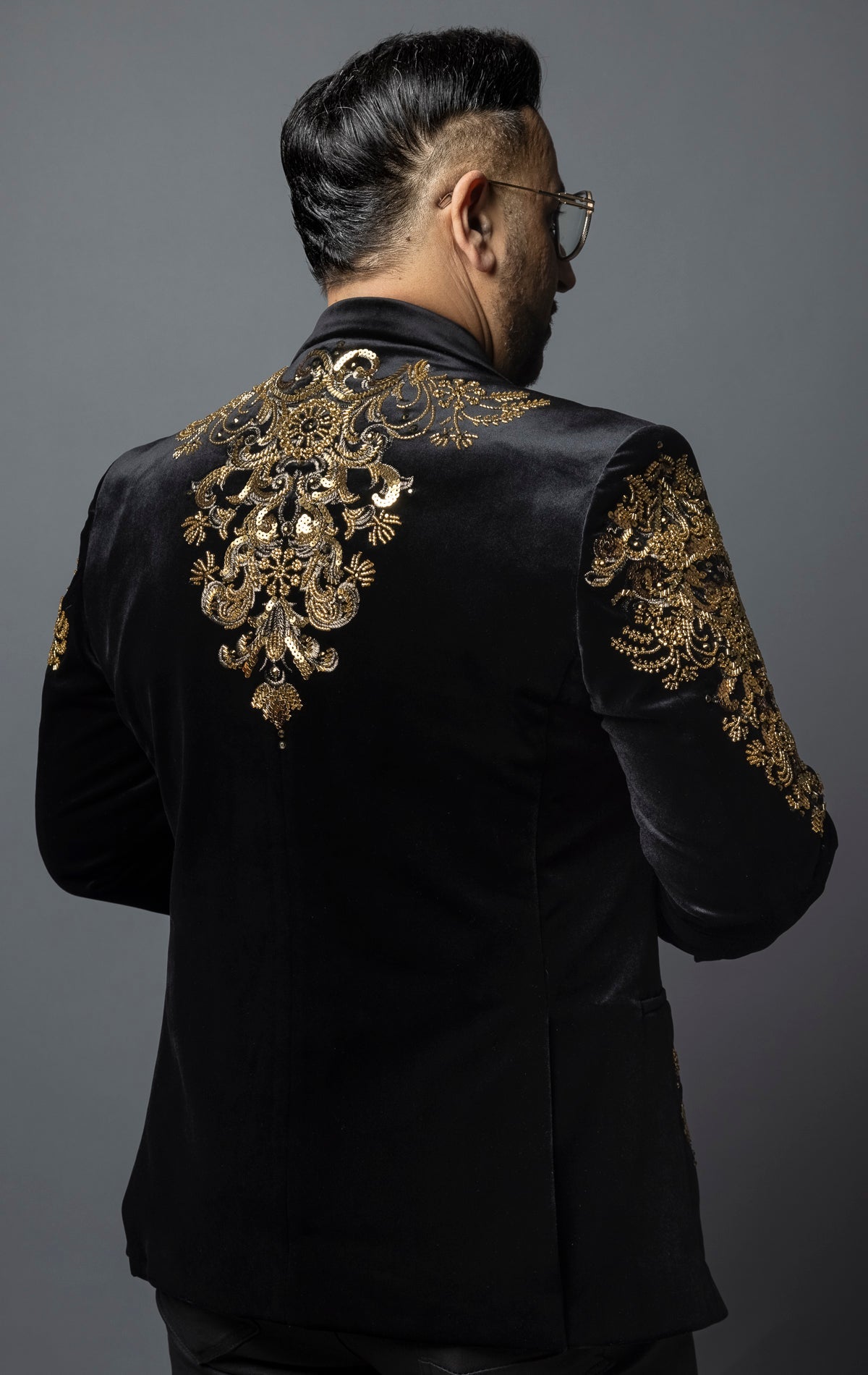 Black, slim-fit velvet blazer adorned with sequins and beads. The blazer has a peak lapel collar, long sleeves, two-button closure, and four-button cuffs. The blazer is made from a blend of 92% regenerated fabric and 8% spandex.