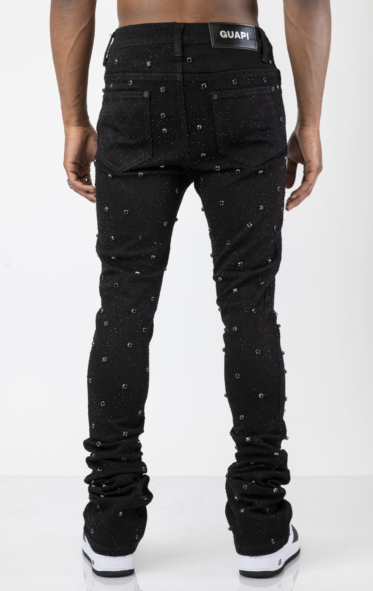 Men's black, tapered-fit jeans with a luxurious cotton-blend fabric (98% cotton, 2% elastane) and custom hardware. The jeans feature subtle laser distressing throughout, delicate diamond embellishments, and a five-pocket design. They stack comfortably above the ankle. 