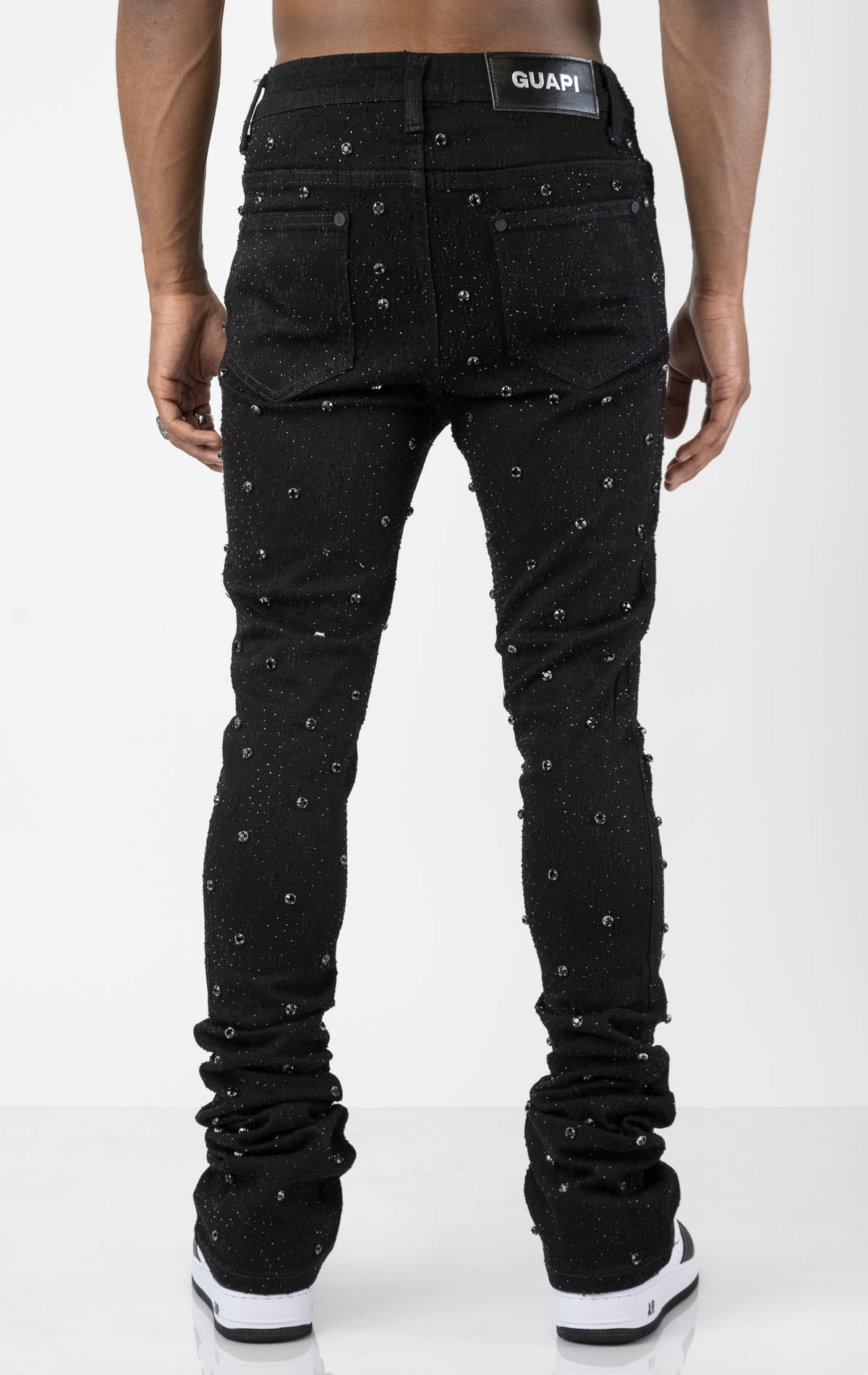 Men's black, tapered-fit jeans with a luxurious cotton-blend fabric (98% cotton, 2% elastane) and custom hardware. The jeans feature subtle laser distressing throughout, delicate diamond embellishments, and a five-pocket design. They stack comfortably abo