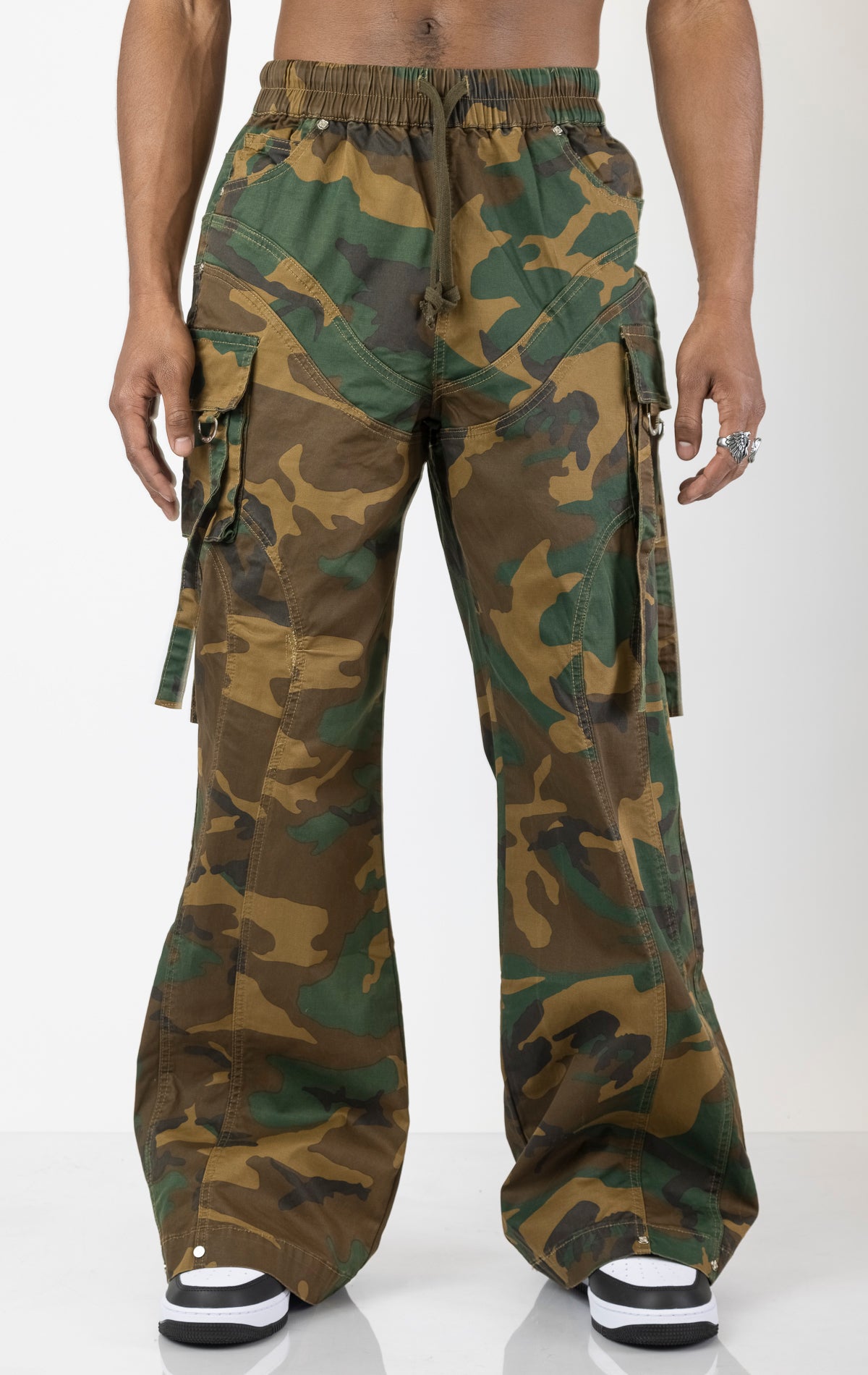Men's baggy cargo pants in camo. The pants feature a wide, relaxed fit from the waist down, paneled construction, spacious cargo pockets with loop closures and functional tightening straps, and custom hardware. Made from a blend of 98% cotton and 2% spandex.  