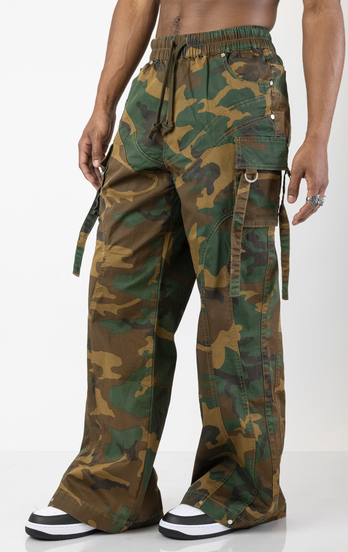 Men's baggy cargo pants in camo. The pants feature a wide, relaxed fit from the waist down, paneled construction, spacious cargo pockets with loop closures and functional tightening straps, and custom hardware. Made from a blend of 98% cotton and 2% spandex.