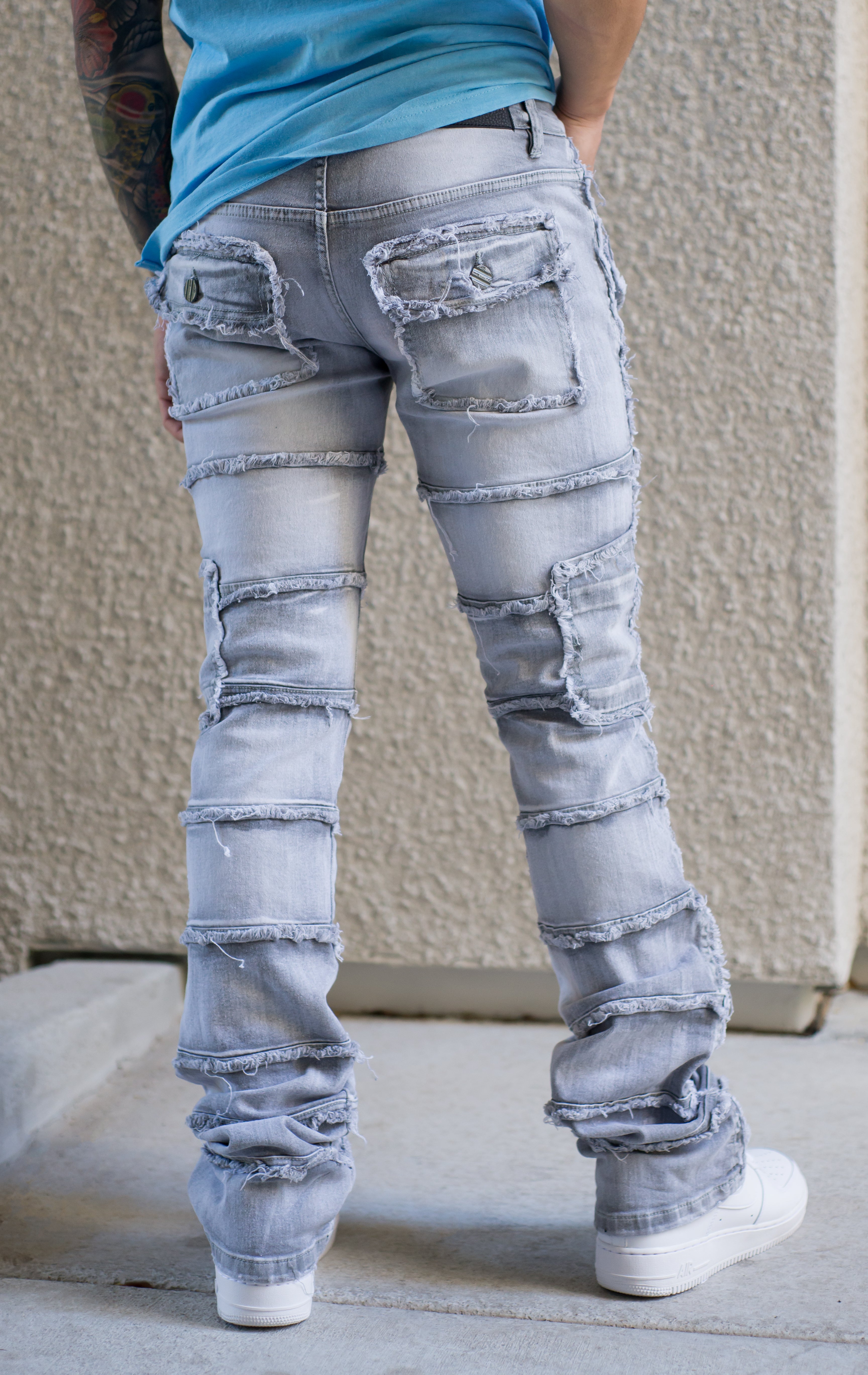 Back side of stacked denim pants, distressed and paneled with a raw finishing