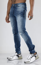 Men's ripped and distressed denim pants in a variety of washes. The pants feature a regular rise, tapered fit from the knee down, open rips at the knees, unique distressing details, and are made from 98% cotton with 2% lycra for stretch