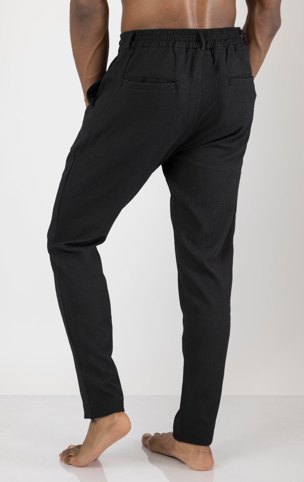 Men's front pleated waffle pants in black. The pants are made from a textured waffle fabric (95% cotton, 5% elastane) and feature a relaxed fit, front pleats, and a comfortable elastic waistband.