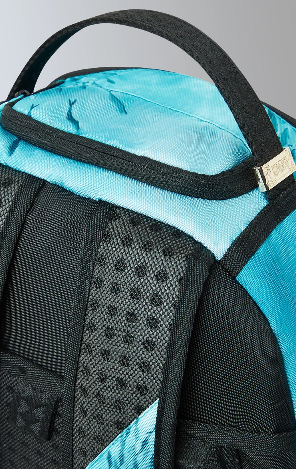 Sprayground backpack with shark graphic, gold zippers and metal hardware featuring multiple compartments and pockets, including a separate velour laptop compartment and a velour sunglass compartment. It has ergonomic mesh back padding, adjustable straps, and a slide-through back sleeve for attaching to carry-on luggage.  The backpack is made from durable 900D polyester fabric.