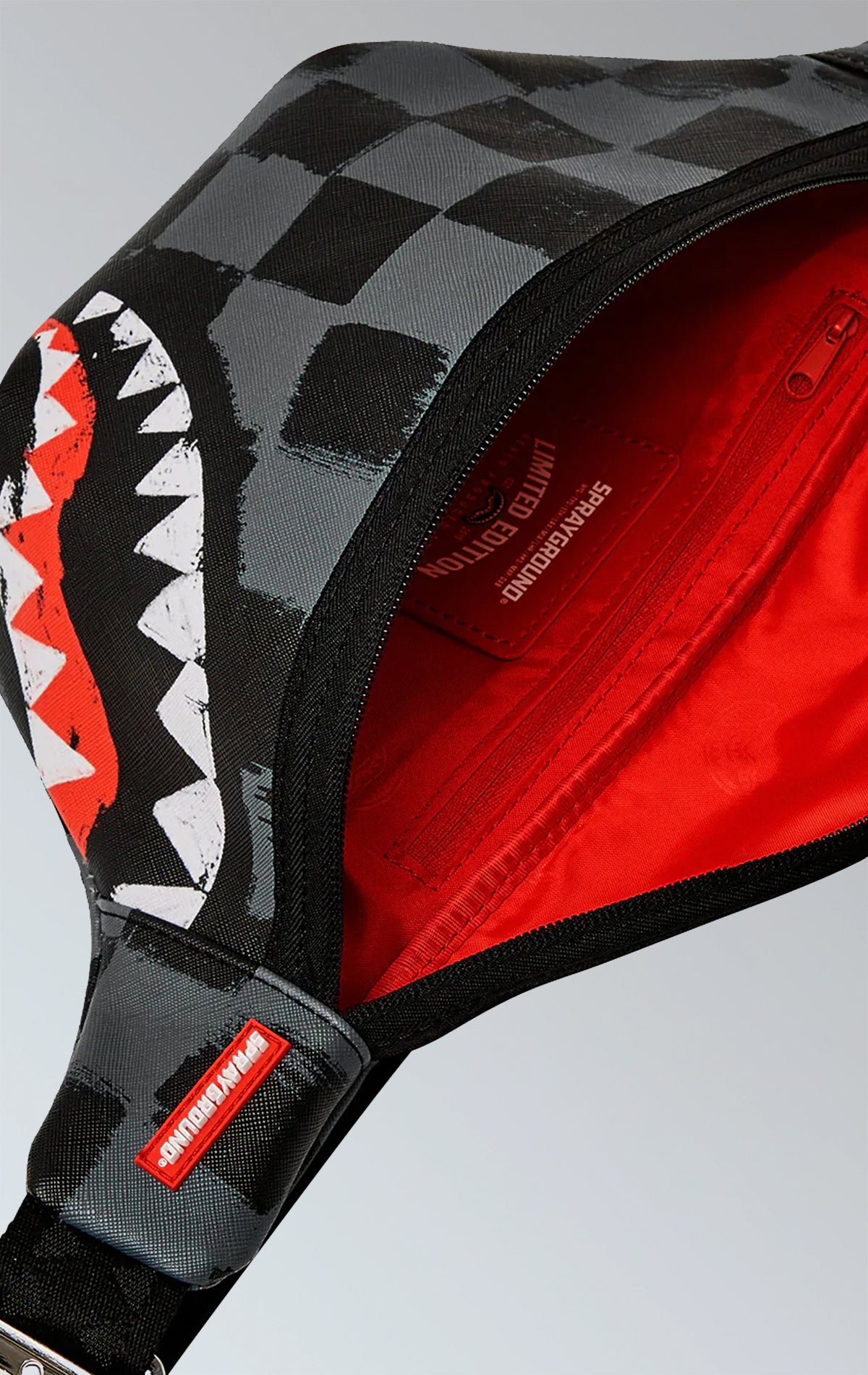 Sprayground crossbody waist bag with a Sharks in Paris design, featuring an adjustable double-sided VSM strap, a red zippered pocket with metal buckle hardware, and durable water-resistant vegan leather construction.