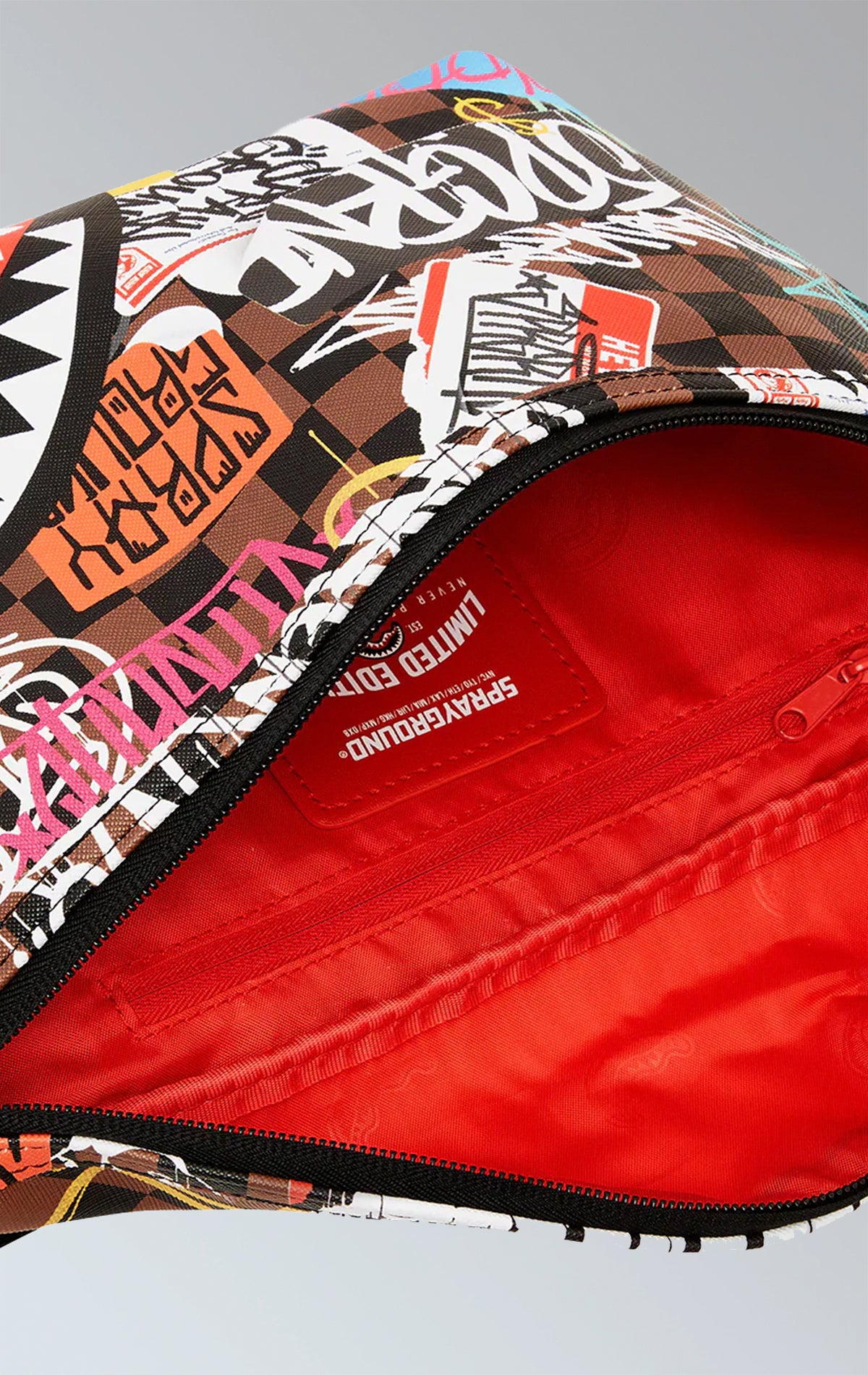 Compact brown Sprayground crossbody in faux leather with a graffiti-inspired print, featuring an adjustable strap and red zippered pocket with buckle closure.