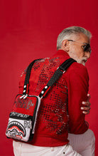 Red Sprayground Vandal Trinity sling bag in durable vegan leather, perfect for essentials like phone, wallet, and sunglasses. Features two front zipper pockets, one back pocket, and side handle.