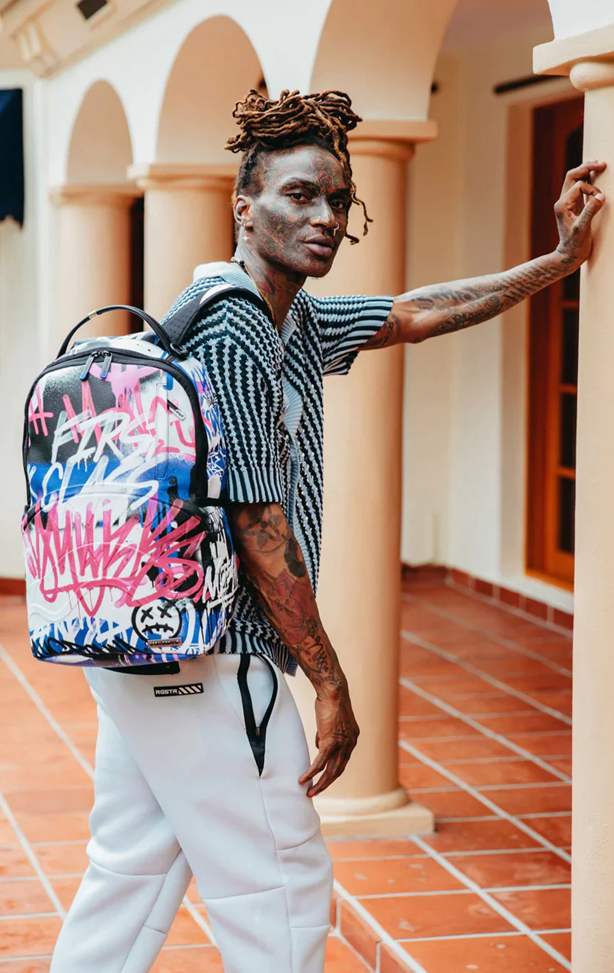 Colorful Sprayground backpack with the iconic Vandal Couture design. Features multiple compartments including a separate velour laptop compartment, side pockets, and a hidden zippered pocket.   Equipped with ergonomic mesh back padding, adjustable straps, and a sliding back sleeve for attaching to carry-on luggage. Made from durable vegan leather.