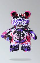 Sprayground purple backpack with Money Bear design, featuring a zippered pocket on the belly, zippered pockets on each arm, a large zippered pocket on the back panel, and adjustable straps. Made from durable water-resistant polyester velour fabric.