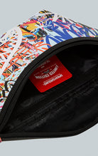 Sprayground Lower East Side Savvy Crossbody in black faux leather. The bag features a compact design, an adjustable double-sided VSM strap for comfortable wear, a red zippered pocket with metal buckle hardware, and dimensions of 7" x 1.5" x 15"